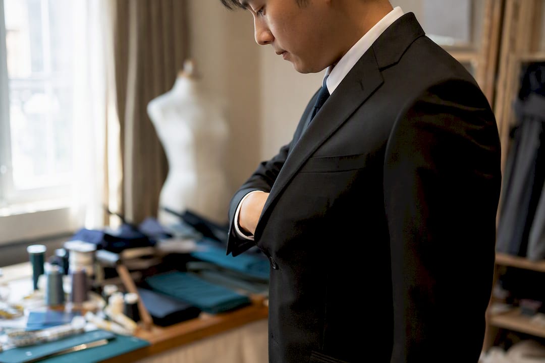 一位亚洲男士穿着扣好的西装外套,正在用拳头测试衣服的合身度。